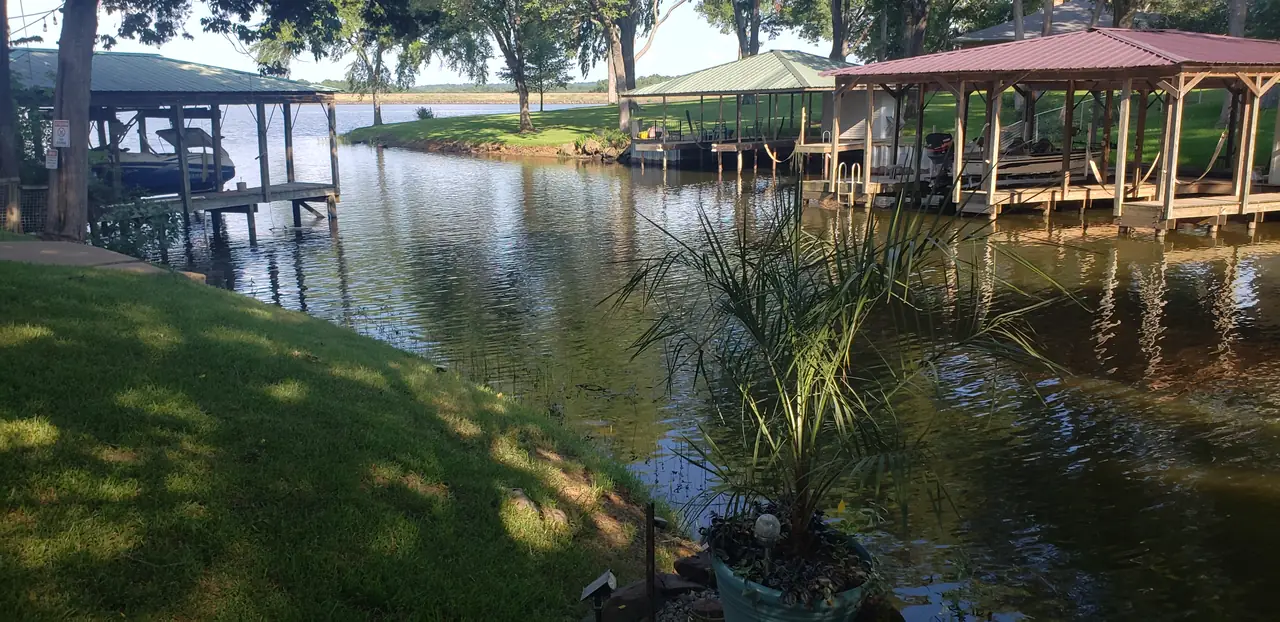 Several covered boathouses spaced along a narrow cove on Lake Palestine, with boats on lifts and a grassy bank