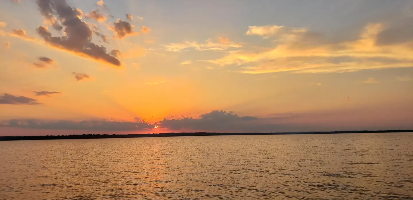 The sun setting over a long, open stretch of Lake Palestine, seen from the water with a low tree line on the horizon.